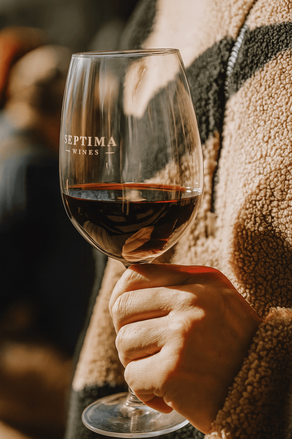 Person holding a glass of red wine labeled Septima Wines, wearing a warm textured jacket.