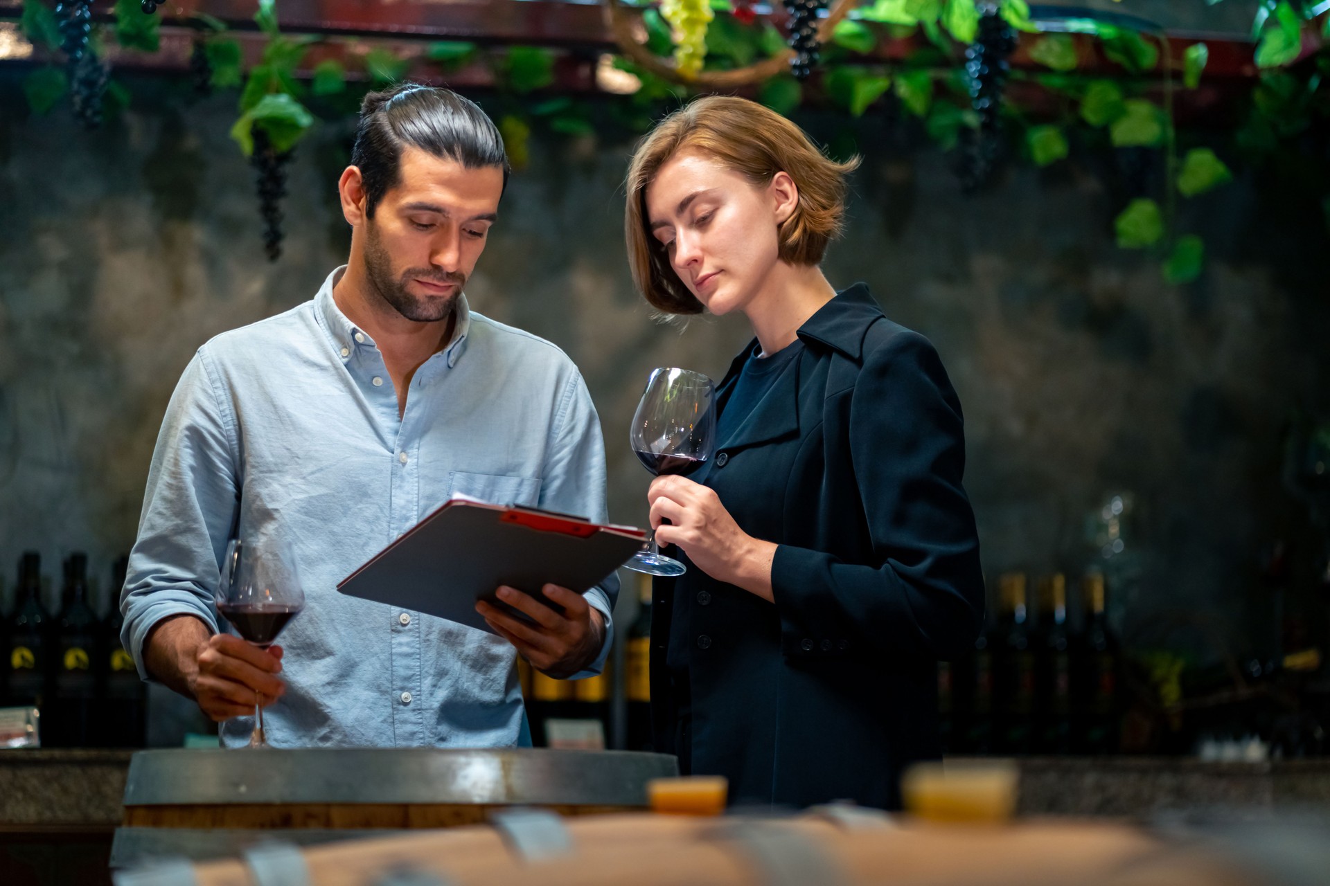 Hombre y mujer sommelier degustando vino tinto en bodega.