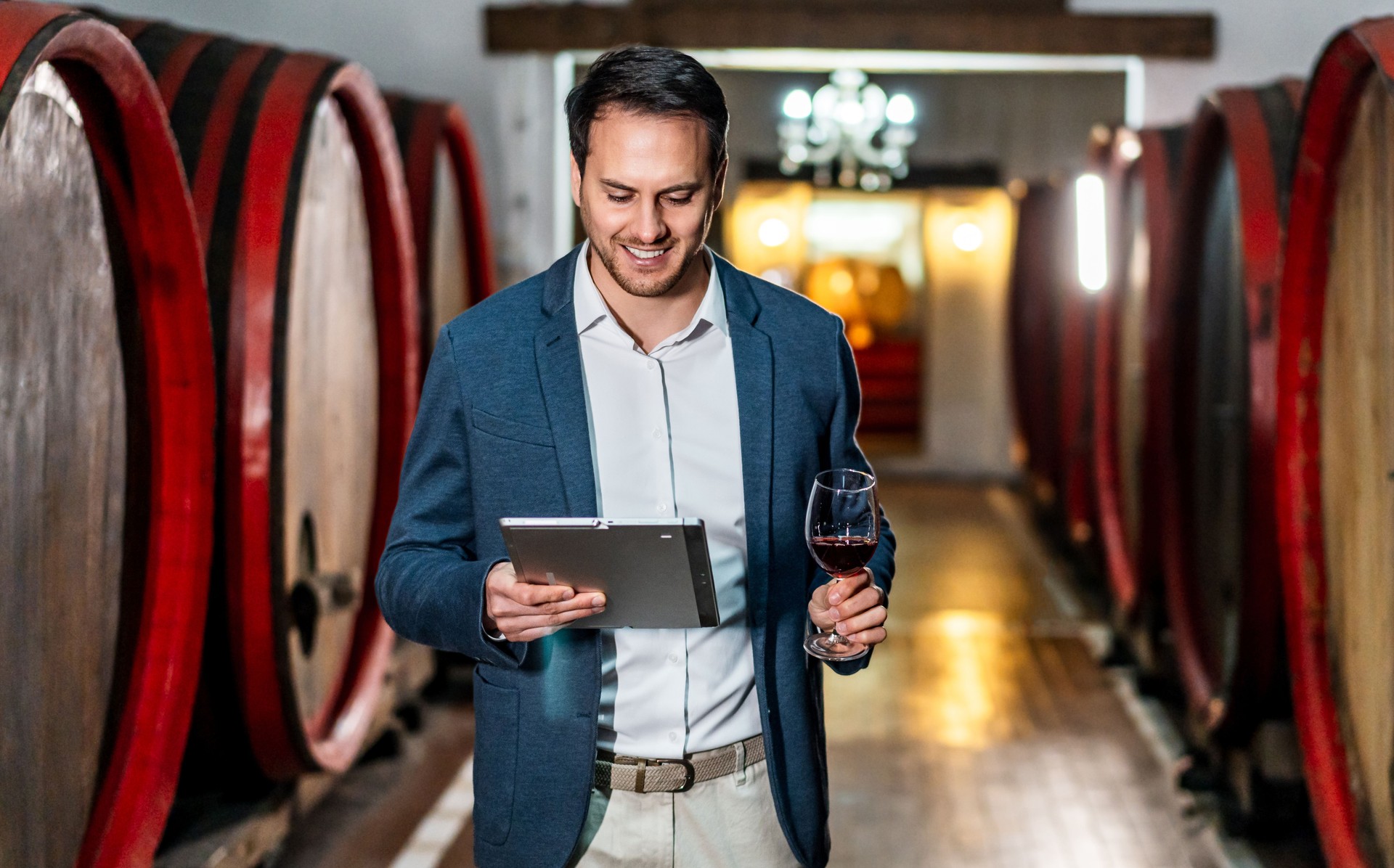 Enólogo usando tableta digital y catando vino en bodega