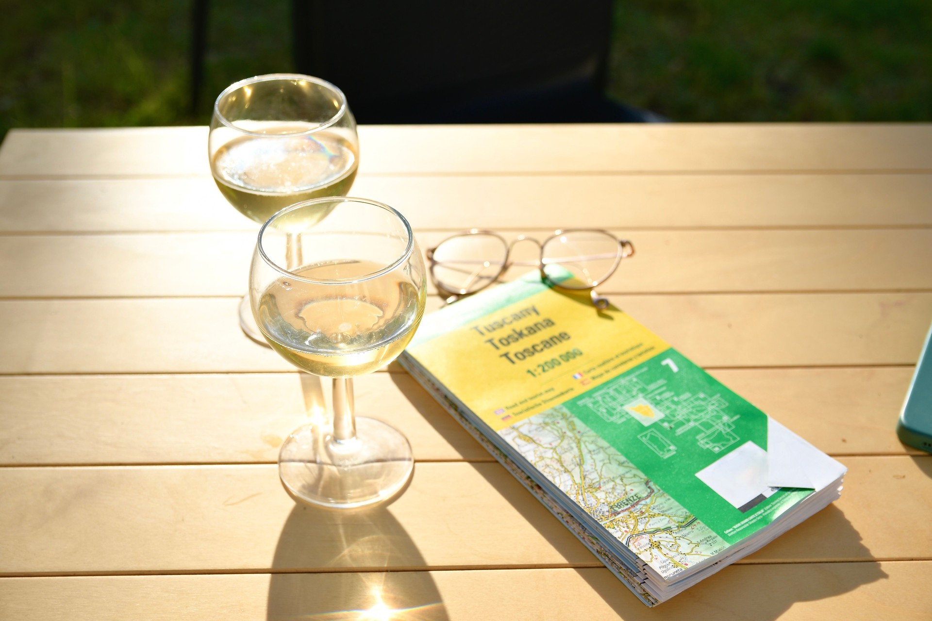 2 glasses of white wine on a small wooden table in a sunny backyard
