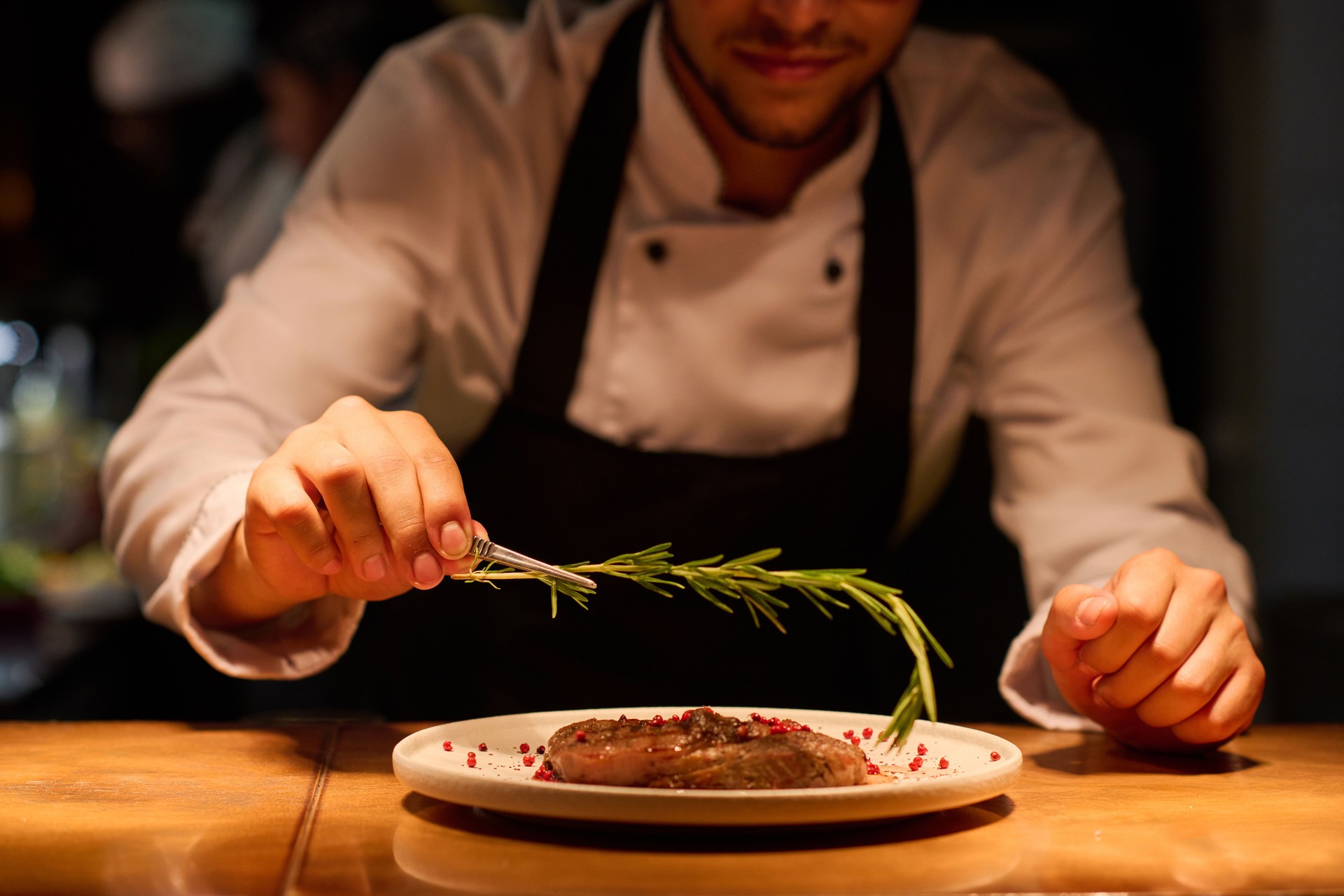 Mano de joven chef poniendo hierba aromática encima de carne asada