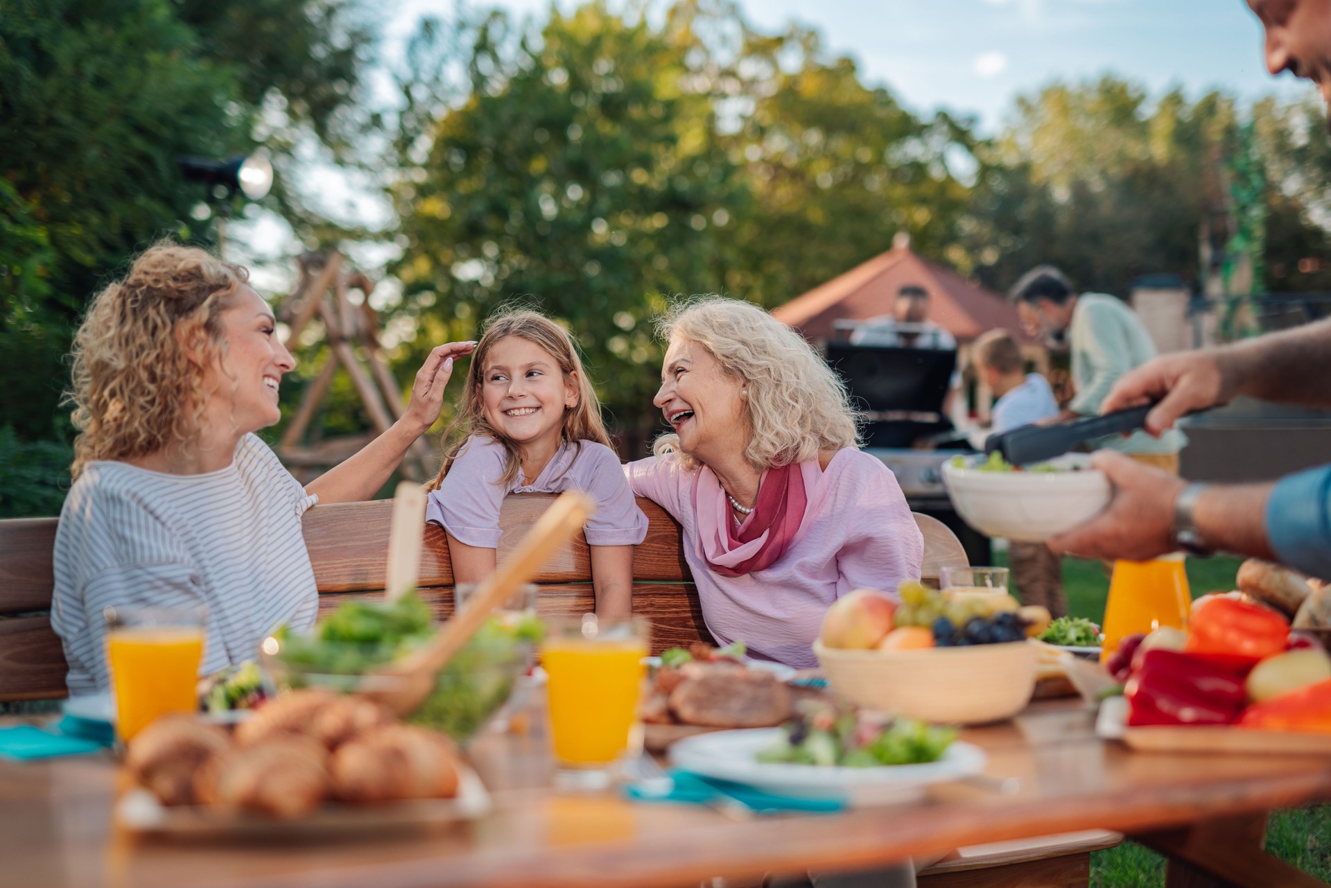 Familia feliz disfrutando de la barbacoa en el patio trasero: abuela, madre e hija compartiendo una risa